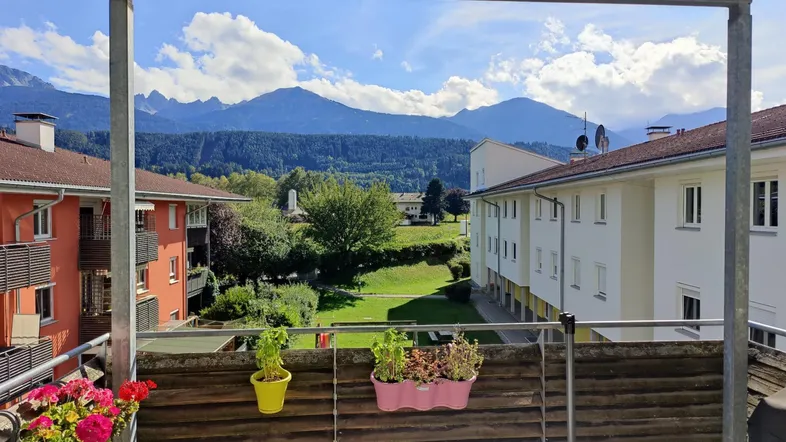 Sonniger Balkon mit Blumentöpfen und einem weiten Blick auf die umliegende Berglandschaft.