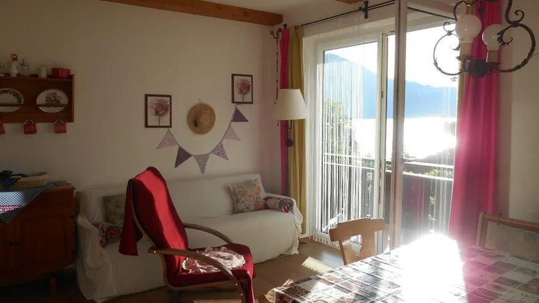 Helles Wohn-Esszimmer mit Holzbalken, Seeblick und Zugang zu einem sonnigen Balkon.