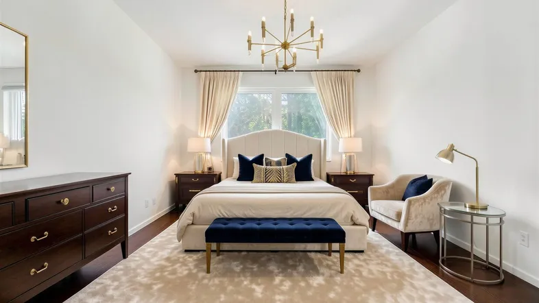 Elegantes Schlafzimmer mit dunklem Holzboden, hellem Teppich und einem großen Bett mit Samtbank.
