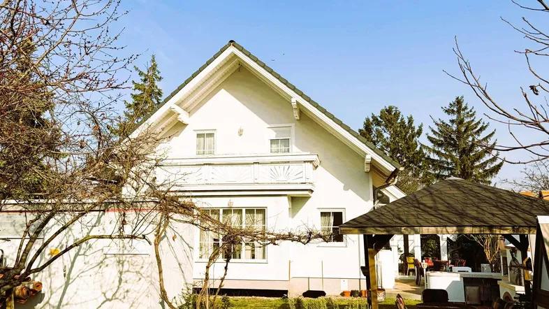 Weißes Einfamilienhaus mit Satteldach, umgeben von einem gepflegten Garten und einem Pavillon.