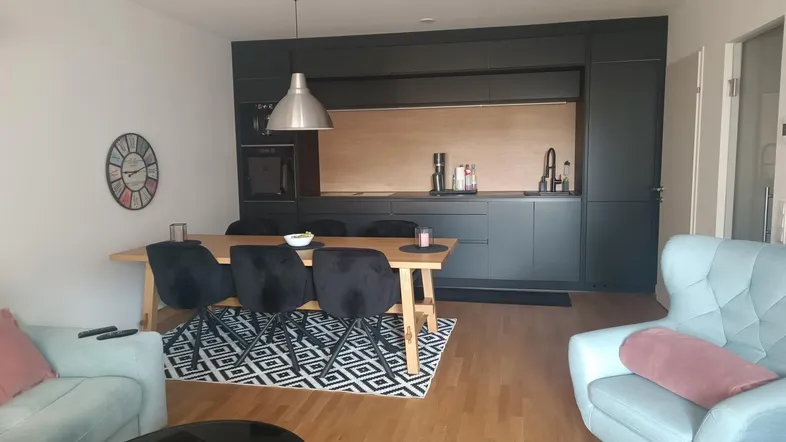 Moderner offener Wohn-Essbereich mit integrierter Küche, Holzboden und gemütlichen Sitzgelegenheiten.