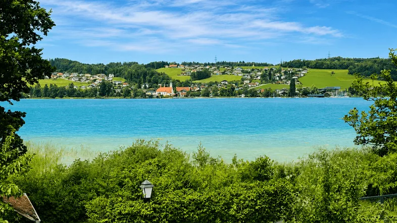 Malerischer Blick auf einen blauen See und ein charmantes Dorf am Ufer unter strahlendem Himmel.