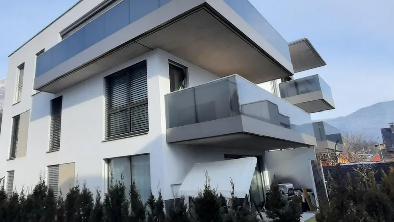 Modernes Mehrfamilienhaus mit mehreren Balkonen, Glasgeländern und einer gepflegten Hecke im Vordergrund.