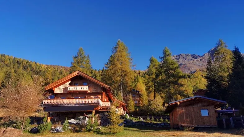 Charmantes Holzhaus im alpinen Stil mit Balkon, umgeben von Wald und Bergen.