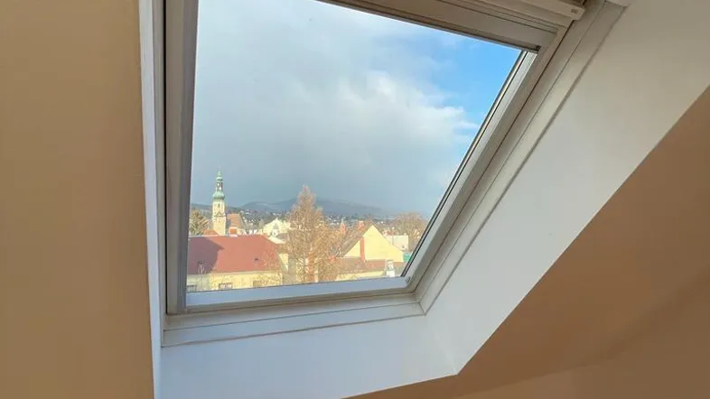 Dachfenster mit Blick auf die Stadt und einen Kirchturm, das viel Tageslicht hereinlässt.
