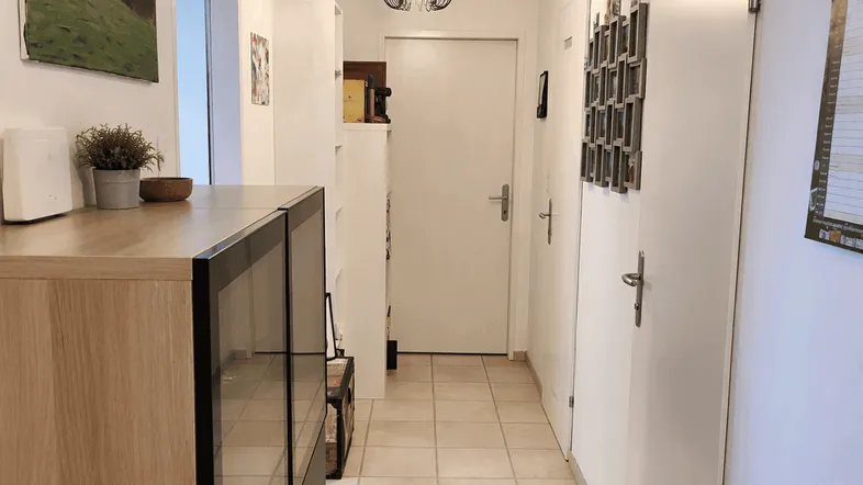 Heller Flur mit modernen Fliesen, einem Holzschrank und einer stilvollen Deckenleuchte.