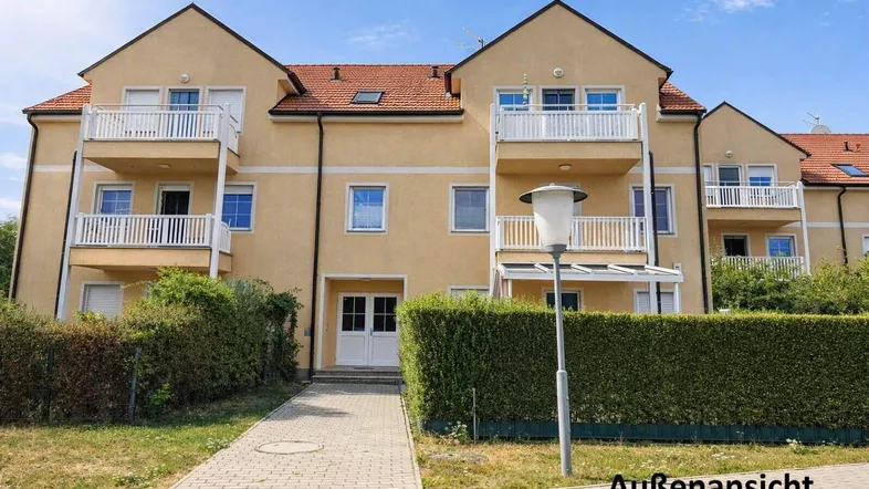 Mehrfamilienhaus mit gelber Fassade, roten Ziegeldächern und mehreren Balkonen in gepflegter Umgebung.