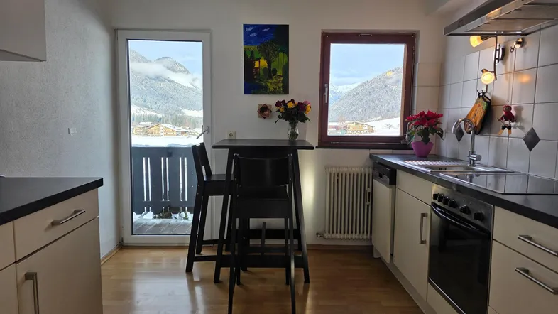 Helle Küche mit Einbaugeräten, Holzboden und Balkonzugang mit Bergblick.