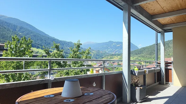 Geräumiger Balkon mit Holztisch und atemberaubendem Bergblick unter blauem Himmel.