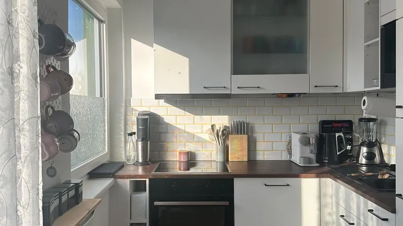 Helle Küche mit weißen Schränken, Holzarbeitsplatte und Fenster, das viel Tageslicht hereinlässt.