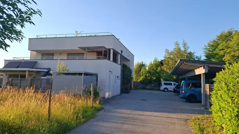 Modernes Mehrfamilienhaus mit Balkonen, Carport und Zufahrt im Sonnenlicht.