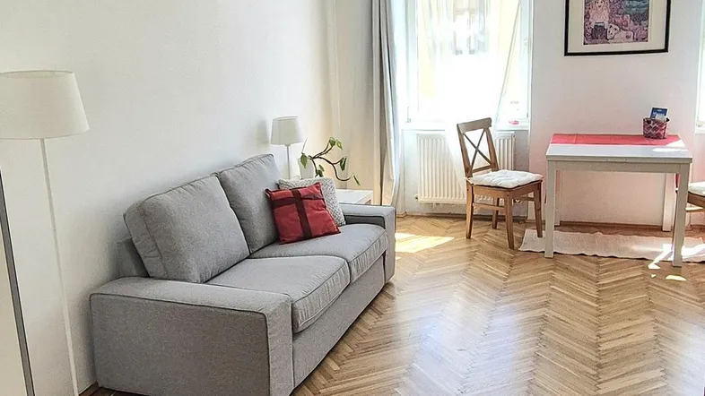 Helles Wohn- und Esszimmer mit Fischgrätparkett, bequemer Couch und einem Esstisch am Fenster.