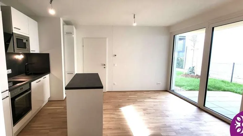 Moderne offene Küche mit Kochinsel, Holzboden und Zugang zu großen Fenstern mit Blick ins Grüne.