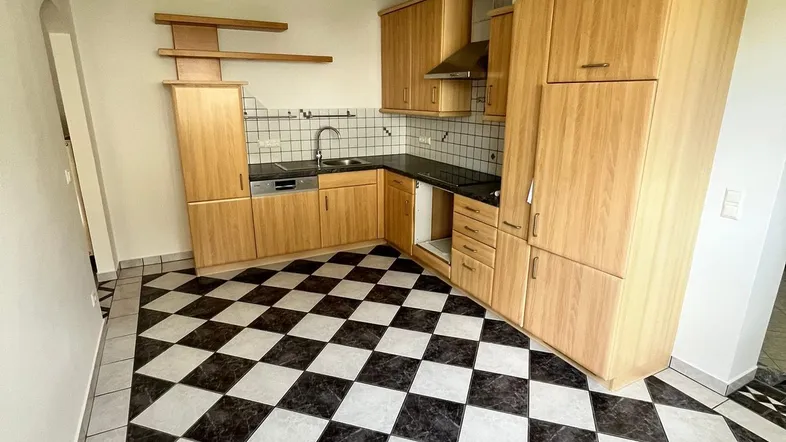 Geräumige Küche mit Holzschränken, schwarzer Arbeitsplatte und auffälligem schwarz-weißem Fliesenboden.