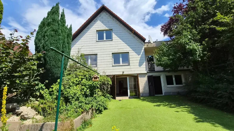 Hinteransicht des Hauses mit einem grünen Garten und Zugang zu den unteren Wohnbereichen.