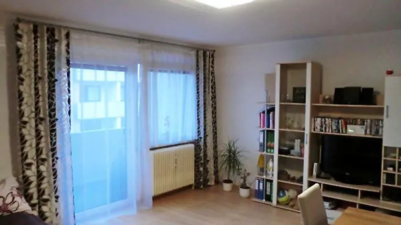 Gemütlicher Wohn- und Essbereich mit Schlafgelegenheit, TV-Möbel und Zugang zum Balkon.