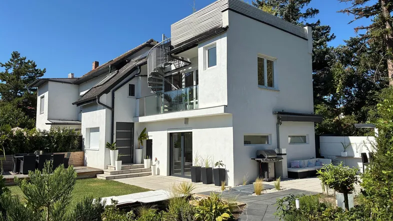 Modernes Haus mit weißer Fassade, gepflegtem Garten, Terrasse und Außentreppe zu einem Balkon.