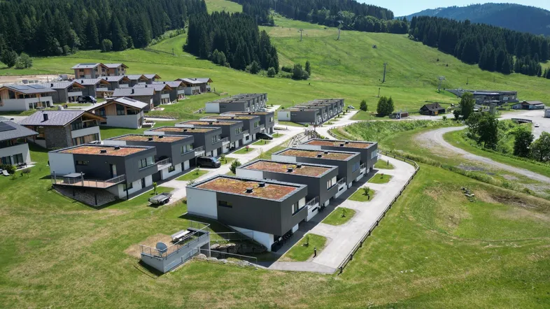 Luftaufnahme einer modernen Wohnanlage mit Flachdächern in einer grünen Berglandschaft.