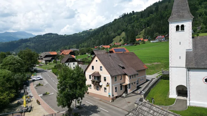 Luftaufnahme eines malerischen Dorfes mit Kirche, Häusern und grünen Hügeln unter blauem Himmel.