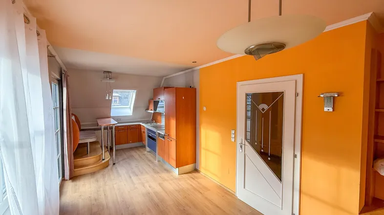 Offener Wohnbereich mit integrierter Küche, Dachschräge und hellem Laminatboden.