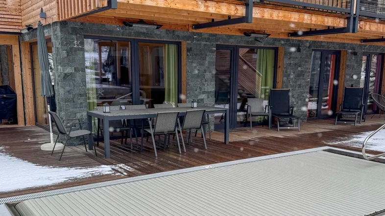 Geräumige Terrasse mit Esstisch, Sitzgelegenheiten und einem abgedeckten Poolbereich im Schnee.