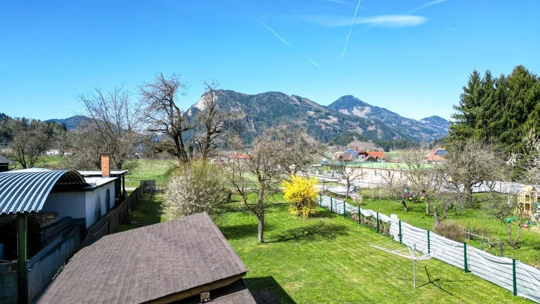 Weitläufiger Gartenbereich mit Rasenfläche und Obstbäumen, umgeben von einer malerischen Berglandschaft.