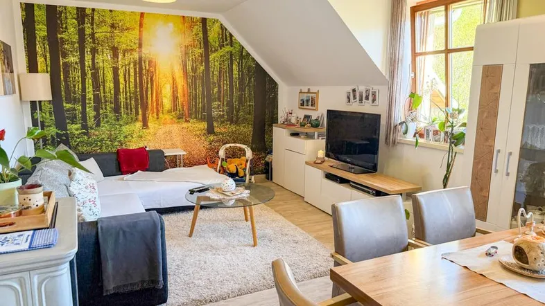 Gemütlicher Wohn- und Essbereich mit Waldtapete, Dachschräge und hellem Interieur.