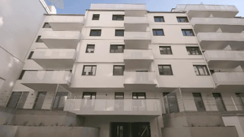 Modernes Mehrfamilienhaus mit weißer Fassade und zahlreichen Balkonen unter blauem Himmel.