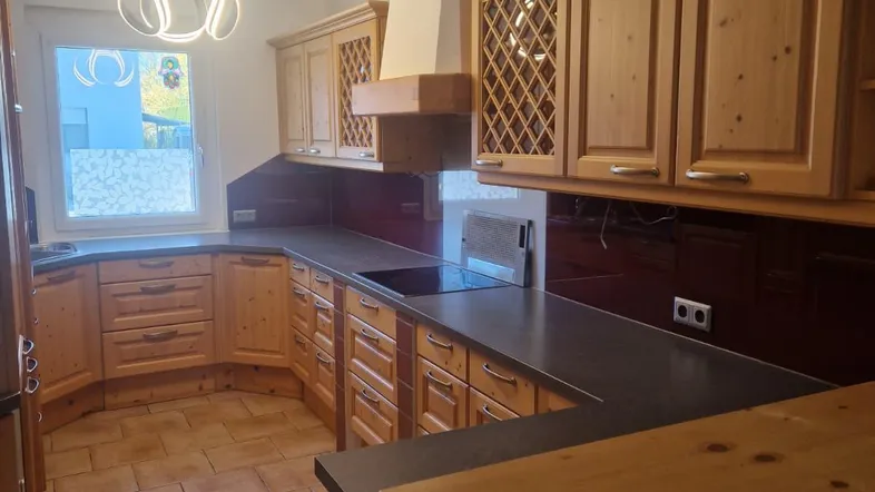 Traditionelle Holzküche mit dunkler Arbeitsplatte, Fliesenboden und modernem Deckenlicht.