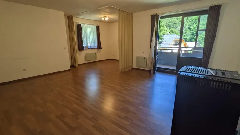 Geräumiges Wohnzimmer mit Laminatboden, Ofen und Zugang zu einem Balkon mit Blick ins Grüne.