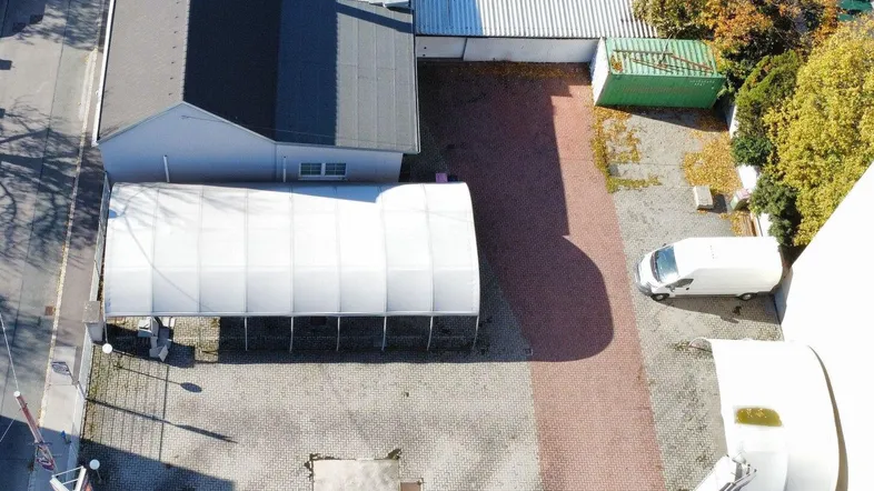 Luftaufnahme eines Gewerbegrundstücks mit mehreren Gebäuden, einer großen Zeltstruktur und gepflasterten Parkflächen.