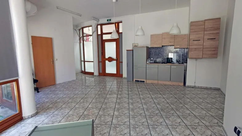 Großer, heller Gewerberaum mit Fliesenboden, integrierter Küchenzeile und hohen Decken.