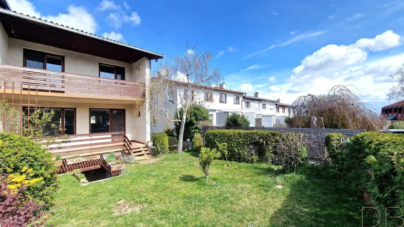Außenansicht eines Reihenhauses mit Garten, Rasenfläche und einer Holzterrasse im Vordergrund.