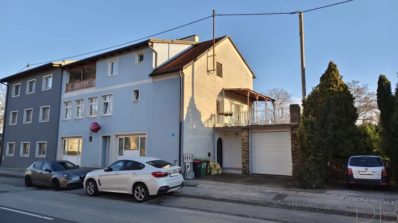 Mehrfamilienhaus mit hellblauer und grauer Fassade, Balkonen, Garage und Stellplätzen an der Straße.