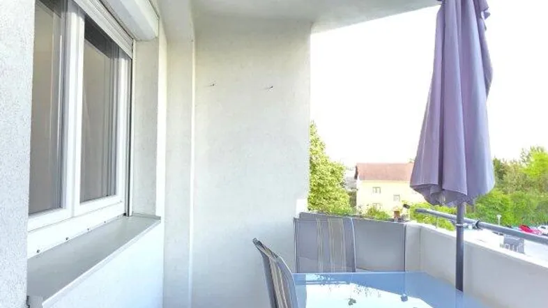 Heller Balkon mit Fliesenboden, einem Tisch, Stühlen und einem Sonnenschirm.
