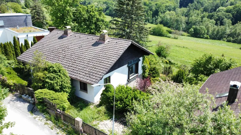 Luftaufnahme eines Einfamilienhauses mit Satteldach, umgeben von viel Grün und angrenzenden Feldern.