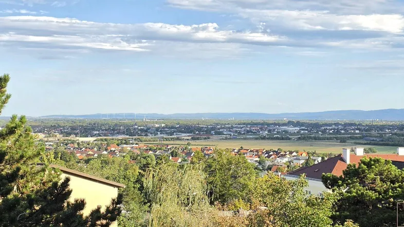 Weitläufiger Ausblick über die Stadt und grüne Landschaft unter einem bewölkten Himmel.