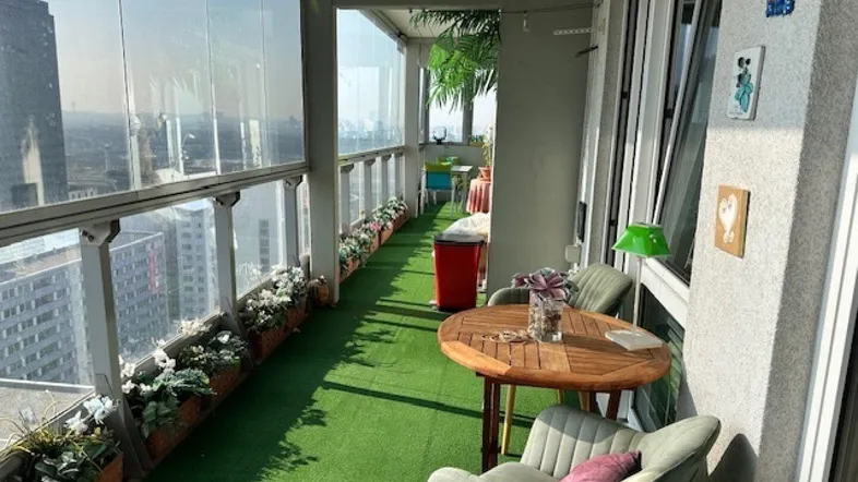 Verglaster Balkon mit Kunstrasen, Sitzgelegenheiten und weitem Stadtblick.