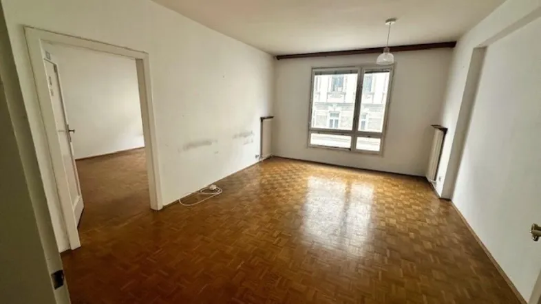 Helles Wohnzimmer mit Fischgrätparkettboden und Blick auf die Stadt durch das Fenster.