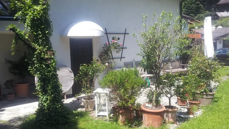 Gepflegter Gartenbereich mit verschiedenen Topfpflanzen und einer kleinen Sitzecke am Haus.