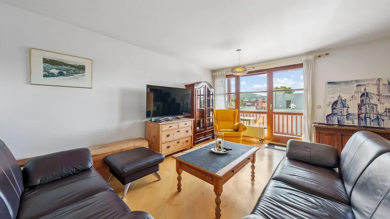 Helles Wohnzimmer mit bequemen Ledersofas, Holzboden und Zugang zum Balkon mit Weitblick.