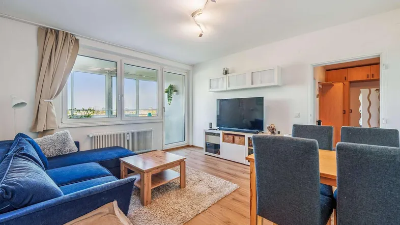 Helles Wohn- und Esszimmer mit Holzboden, blauer Couch und Zugang zu einem Balkon.