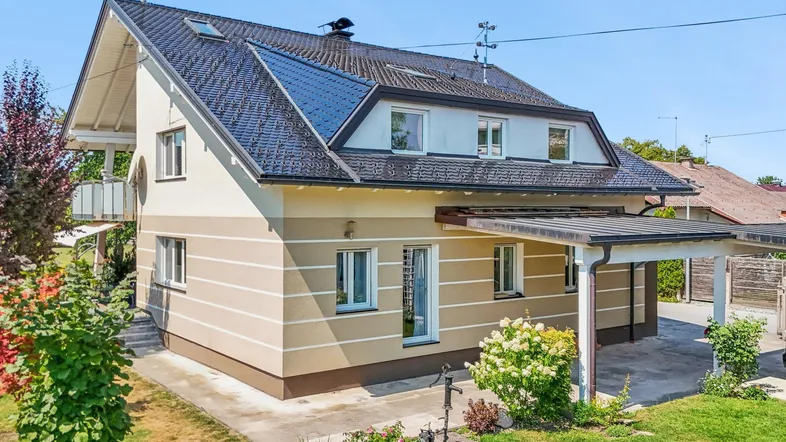 Einfamilienhaus mit Satteldach, beiger Fassade und integriertem Carport auf einem sonnigen Grundstück.