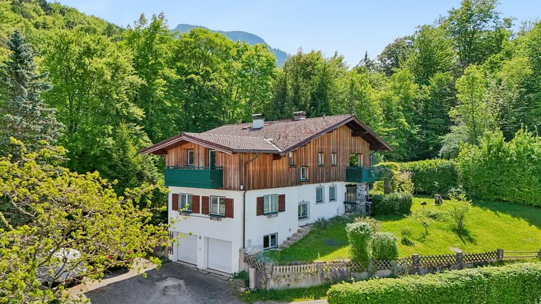 Traditionelles Haus mit Holzbalkonen und weißer Fassade, umgeben von üppiger Natur und Bergen.