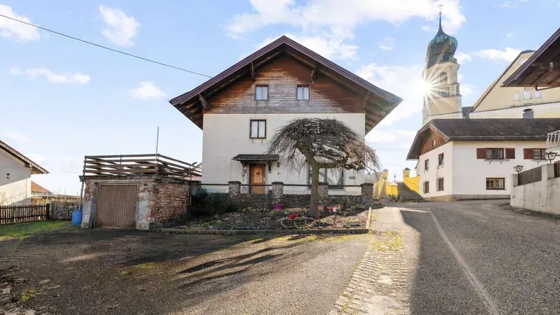 Hausfassade mit traditioneller Architektur und Kirchturm im Hintergrund bei Sonnenschein.