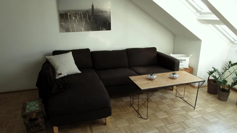 Gemütliches Wohnzimmer im Dachgeschoss mit dunklem Ecksofa, Holztisch und Dachfenstern.