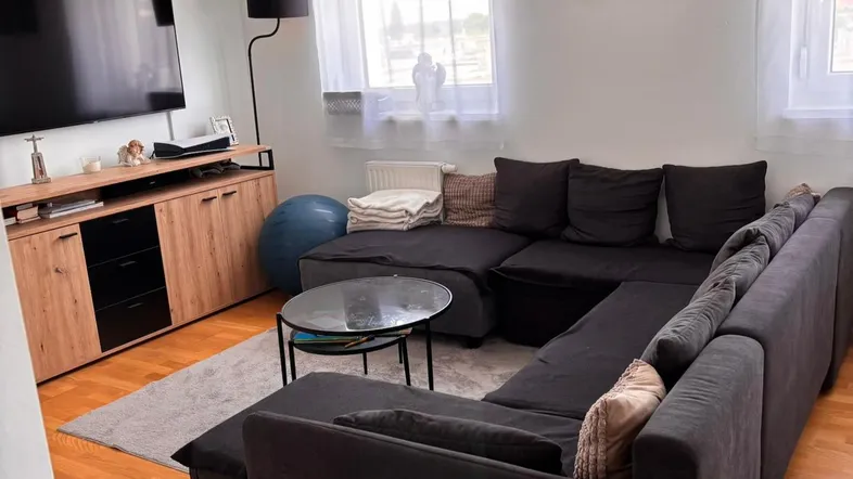 Gemütliches Wohnzimmer mit großem Ecksofa, Holzboden und viel Tageslicht durch die Fenster.