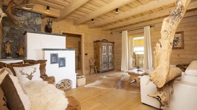 Gemütliches Wohnzimmer im alpinen Stil mit Kachelofen, Holzwänden und Hirschgeweih-Dekoration.