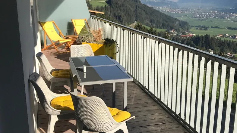 Sonniger Balkon mit Holzboden, Sitzgelegenheiten und atemberaubendem Bergblick.