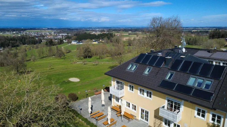 Luftaufnahme des Gebäudes mit Solaranlage auf dem Dach und weitläufiger grüner Landschaft im Hintergrund.